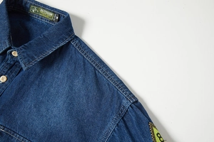 Dettaglio del colletto di una camicia di jeans blu scuro con etichetta e cuciture rinforzate