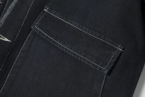 Detail van zwart denim jack met witte contraststiksels en een grote klepzak erop