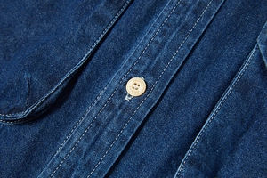 Dettaglio di camicia in denim blu scuro con cuciture bianche a contrasto e bottone