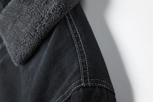 Detail van een zwart spijkerjack met warme grijze fleece kraag en witte contraststiksels