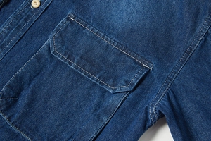 Dettaglio del taschino della camicia in denim blu scuro con doppie cuciture bianche