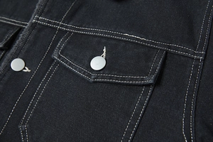 Dettaglio di giacca di jeans nera con cuciture bianche a contrasto e bottone in metallo
