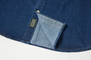 Dettaglio camicia in denim blu scuro con cuciture bianche a contrasto ed etichetta moda