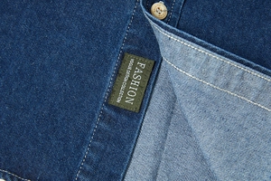 Dettaglio del colletto di una camicia di jeans blu scuro con cuciture e etichetta moda