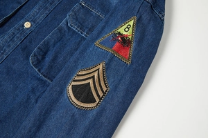 Dettaglio della manica di una camicia di jeans blu scuro con ricami vintage e bottone metallico