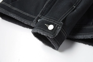 Dettaglio giacca in denim nero con fodera in pile grigio, cuciture bianche e bottoni in metallo