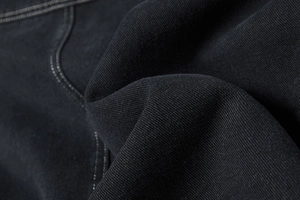 Detailopname van de zwarte denim stofstructuur met witte contrasterende stiksels