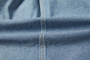 Dettaglio macro del tessuto denim azzurro con robuste cuciture doppie per camicie