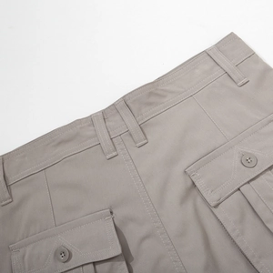 Detail of cargo pants showing grey fabric texture, buttoned pocket, and reinforced stitching