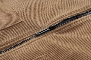 Detail van metalen ritssluiting en geribbelde corduroy textuur op de bruine jas