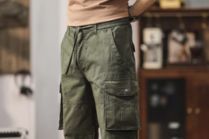 Détail d'un pantalon cargo vert olive avec cordon de serrage et poches à rabat latérales