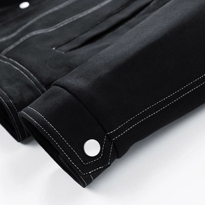 Detailed close-up of a black faux suede jacket sleeve with white contrast stitching and silver button
