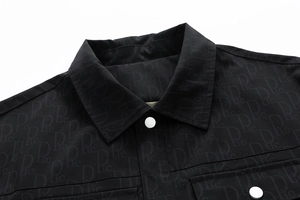 Détail d'une veste noire à revers avec imprimé lettres et bouton métallique argenté