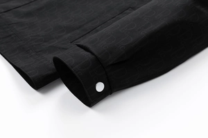 Détail de la manchette de veste noire avec motif monogramme oblique et bouton pression argenté