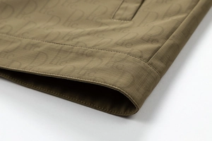 Détail du tissu ripstop olive avec motif monogramme sur l'ourlet de la veste