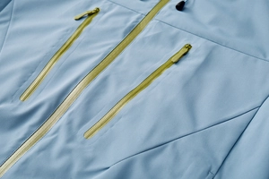 Close-up of waterproof fabric and contrast yellow zippers on light blue outdoor jacket