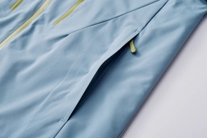 Detail of light blue outdoor jacket showing waterproof zipper with lime green puller cord