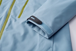 Detail of adjustable windproof cuffs and lime green waterproof zipper on blue outdoor jacket