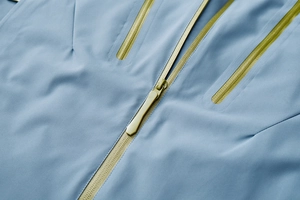 Close-up of light blue outdoor jacket with neon green waterproof zippers and technical fabric