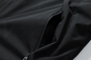 Detail der wasserdichten Outdoor-Jacke mit schwarzem Geometrie-Muster und Reißverschlusstasche