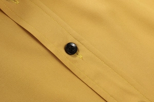 Dettaglio ravvicinato di una camicia da uomo giallo senape con cuciture di qualità e bottone