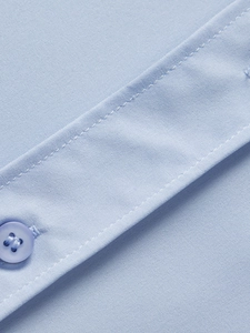 Makroaufnahme eines hellblauen Hemdes mit feiner Stoffstruktur und Nahtdetails am Knopf
