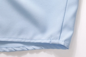 Detailed close-up showing neat hem stitching on light blue cotton fabric of a shirt