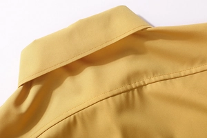 Detail of a men's yellow long-sleeved shirt showing collar stitching and woven texture