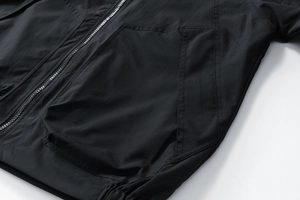 Détail d'une veste noire coupe-vent avec fermeture éclair en métal et grande poche géométrique
