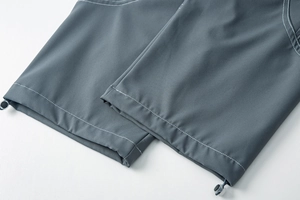 Détail du pantalon cargo gris montrant l'ourlet à cordon et coutures contrastées