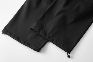 Dettaglio dell'orlo con coulisse regolabile e fibbia su pantaloni tattici neri impermeabili