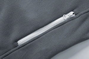 Close-up of thick fleece fabric texture and smooth resin zipper on a warm gray jacket