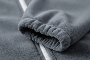 Detail of dark grey fleece jacket featuring elastic cuffs and contrast white zipper closure