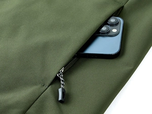 Close-up of olive green outdoor vest side pocket with zipper and phone inside