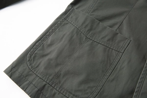 Dettaglio di un blazer in cotone verde scuro con una grande tasca a toppa e doppia cucitura