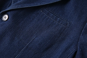 Détail macro d'une veste de costume en denim bleu avec texture à chevrons et revers