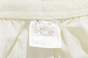 Detailed macro shot of elastic waistband with fabric label on off-white nylon shorts