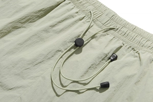 Detail of adjustable elastic waistband with drawstring and toggle on sage green shorts