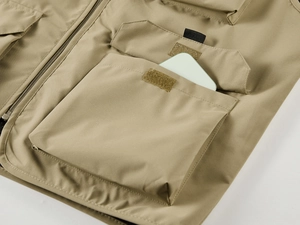 Détail du gilet d'extérieur kaki montrant une grande poche velcro contenant un téléphone