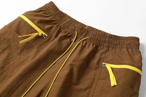 Detail of elastic waist with yellow drawstring and zipper pocket on brown cargo shorts