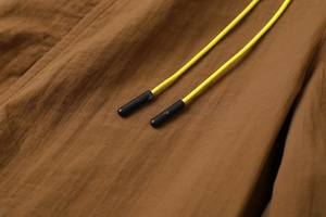 Macro detail of tan nylon fabric with a bright yellow drawstring and matte black aglets
