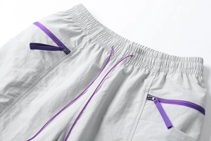 Detail of light gray cargo shorts with purple drawstring waist and zip pockets