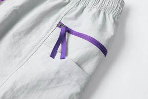 Detail of light gray tech shorts featuring a purple zipper pocket and elastic waistband