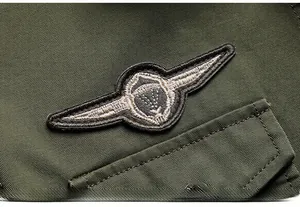 Dettaglio del badge ricamato con ala e bottone in metallo su camicia di cotone verde militare