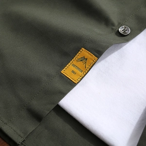 Close-up of army green outdoor shirt detail featuring woven patch and brand button