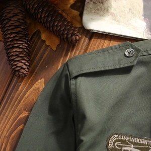 Detail view of army green shirt featuring epaulettes, metal buttons and embroidered patches