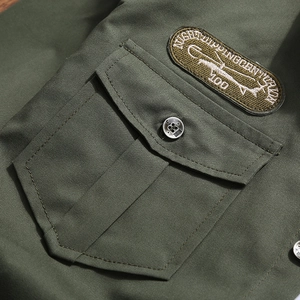 Close-up of military green work shirt featuring an embroidered patch and buttoned flap pocket