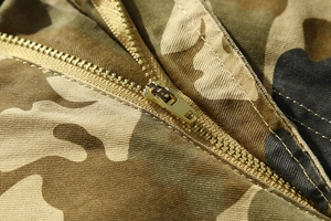 Detail view of durable camouflage cotton fabric and robust brass zipper on cargo shorts
