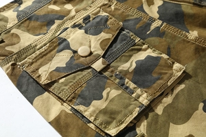 Macro detail of camouflage cotton cargo shorts showing flap pocket and metal button