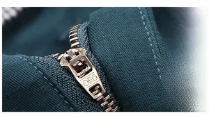 Detail view of durable vintage brass metal zipper with engraved OFC logo on dark fabric